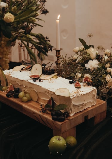 A sheet style wedding cake with white icing, surrounded by fruit and white and green flowers