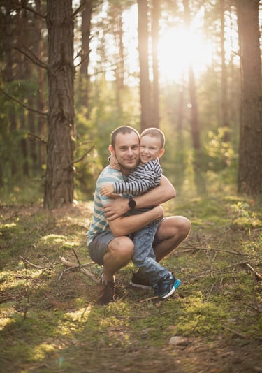 Šeimos fotosesijos akimirka - tėtis ir sūnus miško fone apsikabinę