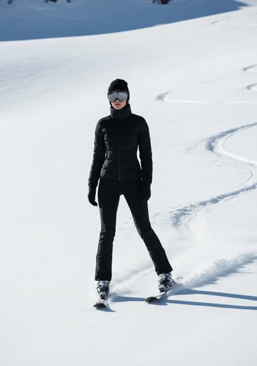A woman skiing on a sunlit slope wearing a form-fitting black thermal ski suit, a black beanie, and 