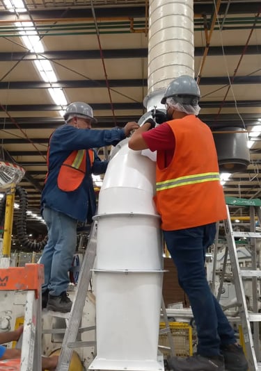 Dos trabajadores industriales con chalecos de seguridad instalando un sistema de ducto de extracción