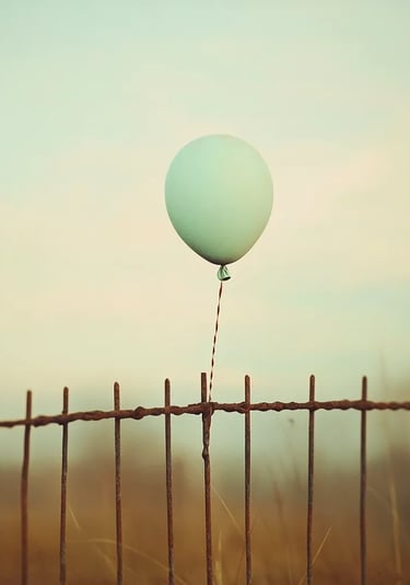Ballon vert pâle flottant au-dessus d’une vieille clôture rouillée, ambiance vintage et mélancolique.