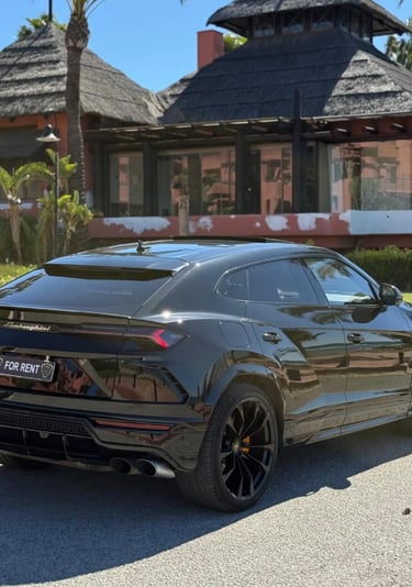 Luxury black Lamborghini Urus SUV for rent parked in front of a tropical resort villa.