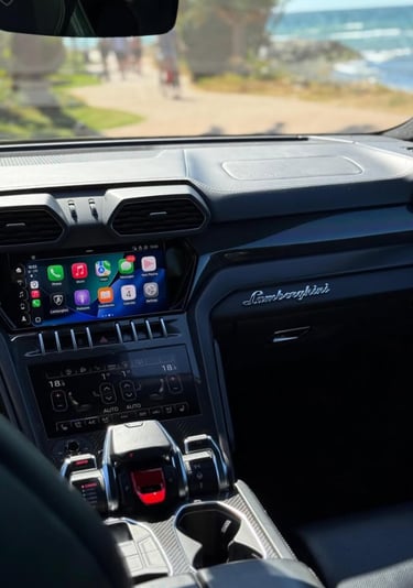 Interior view of a luxury Lamborghini Urus dashboard featuring Apple CarPlay and carbon fiber trim.