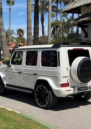 White Mercedes-Benz Brabus G-Wagon luxury SUV parked on a sunny street with palm trees.