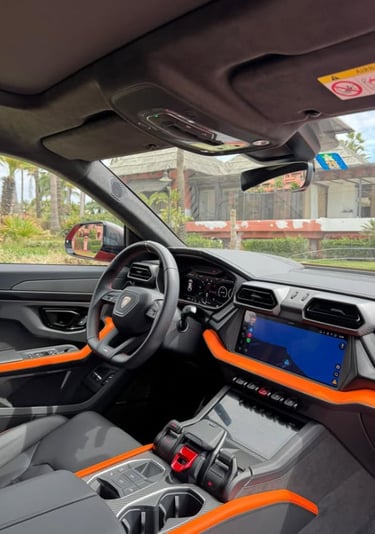 Modern interior of a Lamborghini Urus featuring black leather and orange accents with a digital cockpit.