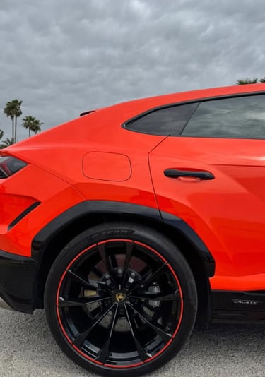 Side profile of a bright orange Lamborghini Urus luxury SUV with black rims and red accents.