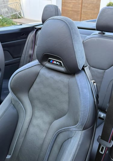 Close-up of a black leather BMW M4 convertible sport bucket seat with Alcantara trim and emblem.