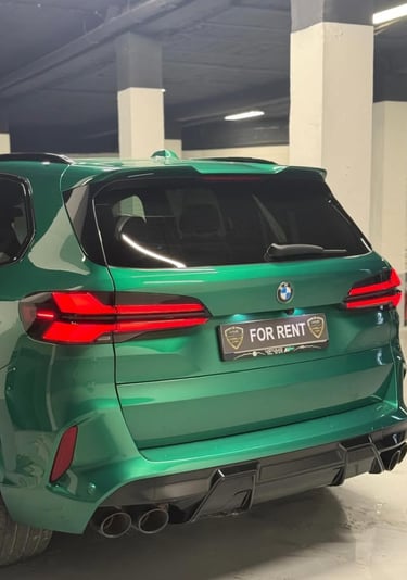 Rear view of a metallic green BMW X5 luxury SUV for rent in an indoor parking garage.