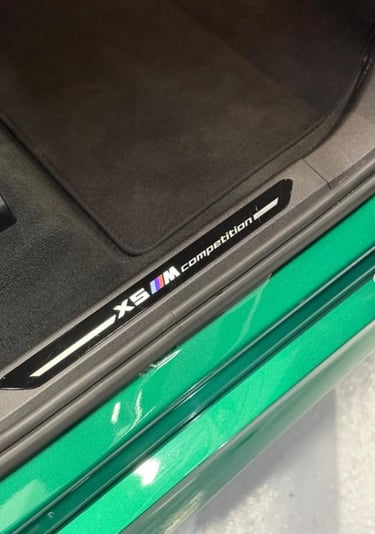 Close-up of a BMW X5 M Competition door sill plate with the M logo on a green luxury SUV.