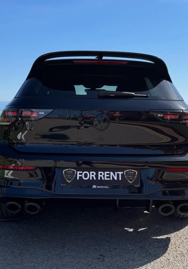 Rear view of a black Volkswagen Golf for rent parked by the ocean on a sunny day.