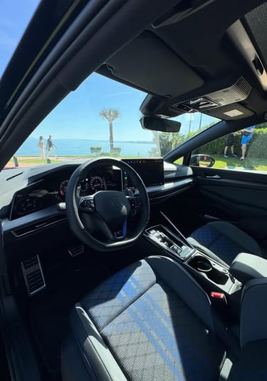 Interior view of a modern Volkswagen Golf R dashboard and cockpit overlooking a sunny beach.