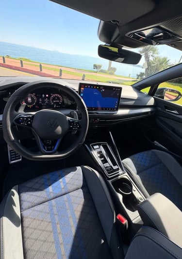 Interior view of a modern Volkswagen Golf with blue accent seats and digital cockpit dashboard parked by the sea.
