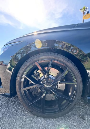 Close-up of a black sports car wheel featuring Bridgestone Potenza tires and gloss black alloy rims.