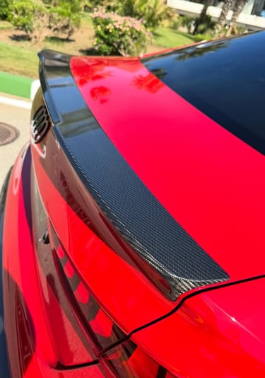 A red Audi sedan featuring a custom carbon fiber trunk spoiler for enhanced vehicle aerodynamics.