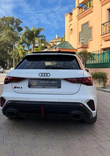 Rear view of a white Audi RS3 sportback luxury car rental parked in front of a villa.