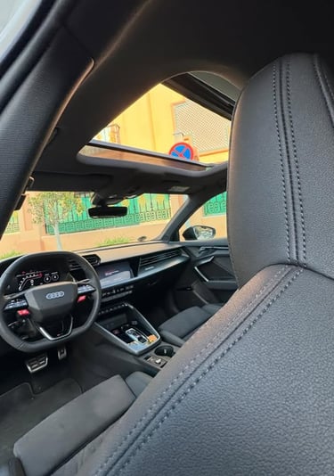 Interior view of an Audi luxury car with black leather seats and an open panoramic sunroof.