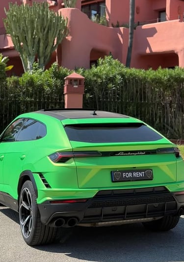 A bright green Lamborghini Urus luxury SUV for rent parked in front of a pink Mediterranean style building.