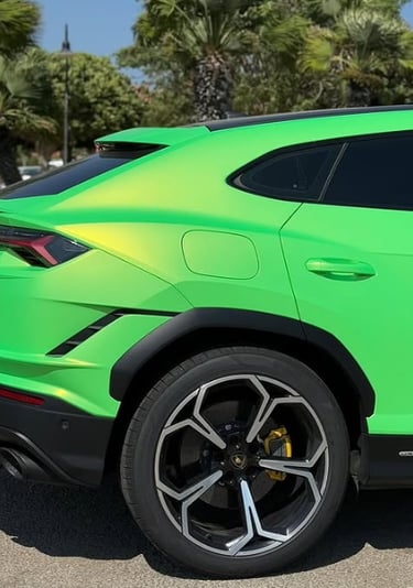 Side view of a bright lime green Lamborghini Urus SUV parked outdoors near tropical palm trees.