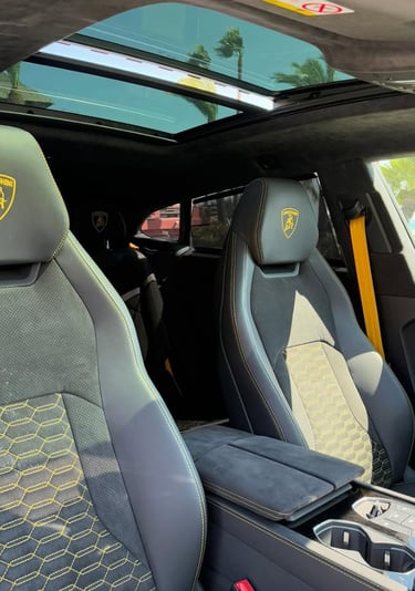 Interior of a luxury Lamborghini Urus featuring black leather seats with yellow stitching and panoramic sunroof.