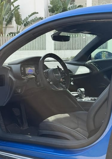 Interior view of a blue Audi R8 sports car showing the black leather seats and luxury dashboard.