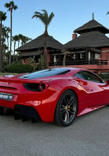 Red Ferrari 488 luxury sports car parked in front of a tropical resort with palm trees.