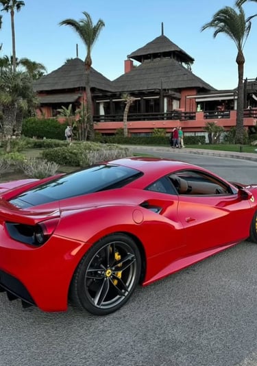 Red Ferrari 488 GTB luxury sports car parked in front of a tropical resort with palm trees.
