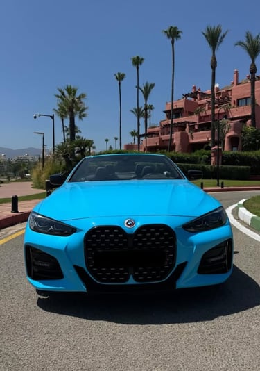 Front view of a bright blue BMW convertible parked on a tropical road with palm trees.
