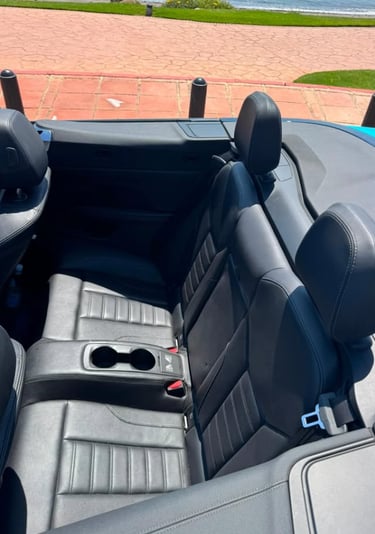Rear black leather seats and cup holders in a luxury convertible car parked near the coast.