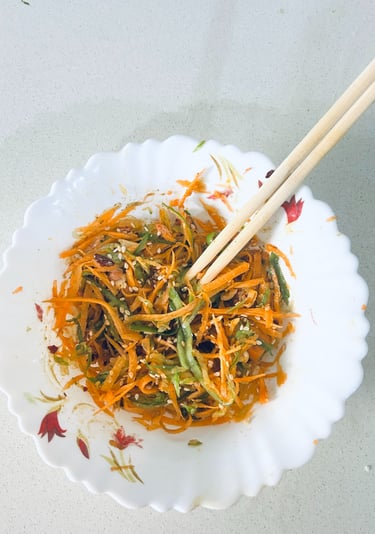 Fresh carrot and green pepper slaw with sesame seeds in a white bowl with wooden chopsticks.