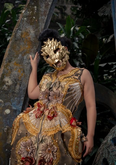 A person in a golden animal mask and ornate floral dress posing against stone ruins in a garden.