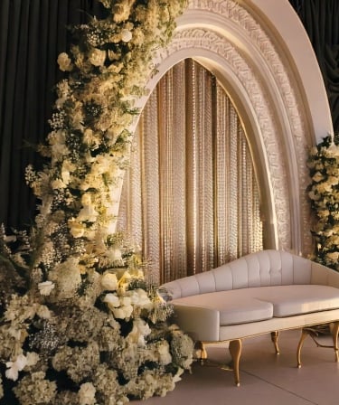 Elegant wedding stage in dubai decor with a white sofa, ornate arch, white floral arrangements.