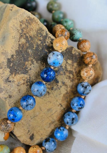 Collar mala de cuentas de gemas de cianita azul natural y jaspe, colocado sobre una piedra rústica.