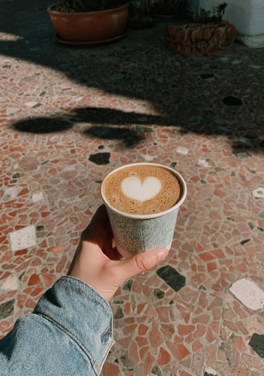 Hand holding a takeaway coffee with heart latte art, representing a thoughtful coffee gift moment.