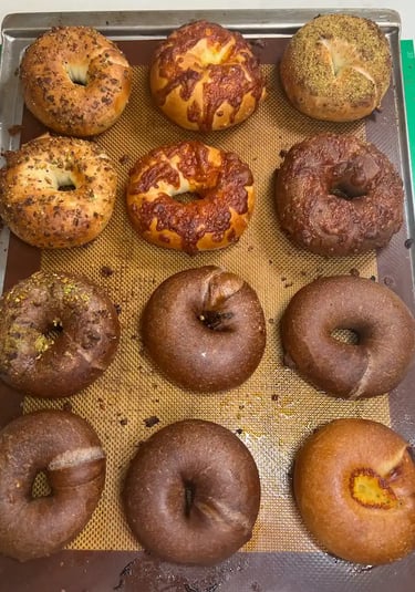 OneDo Workshop 課堂作品展示，一款手工 Bagel 配上芝麻與 芝士餡料， 還有朱古力和開心果餡料背景為學生設計裝飾卡，展現烘焙創作與個人化風格。
