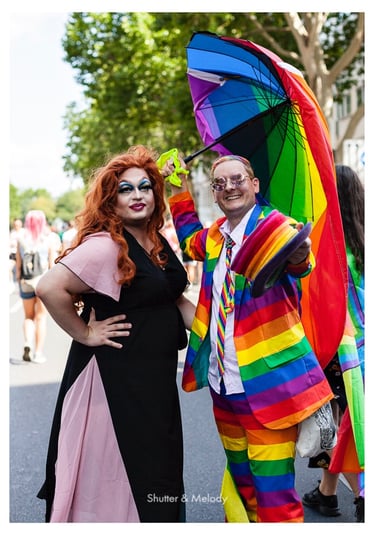 Eine Drag Queen und ein Mann mit Regenbogenanzug, Hut und Regenschirm bei der Christopher Street Day