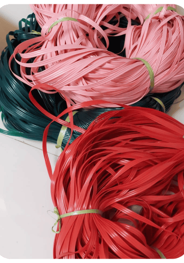 Colorful recycled plastic weaving strips in red, pink, and green prepared for handmade woven bag crafting at Craftvitas