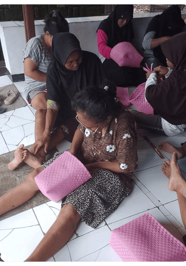 Artisan weaving a pink jali jali plastic woven bag by hand at Craftvitas Indonesia.