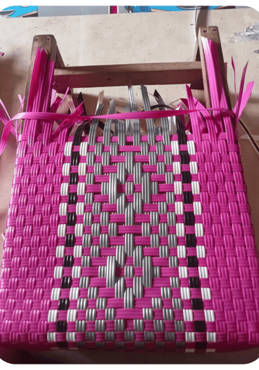 Early weaving process of a pink patterned handmade plastic woven bag at Craftvitas Indonesia.