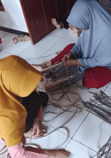 Handmade jali jali woven bag frame being prepared by artisans using recycled plastic weaving strips.