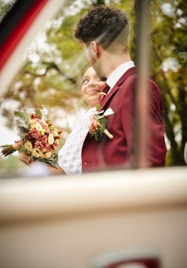 a bride and groom standing in front of a car