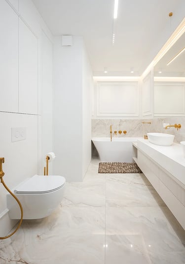 Jasna łazienka z wanną wolnostojącą, umywalką, podwieszaną toaletą i złotą armaturą.