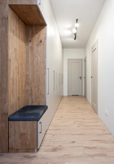 Wąski korytarz z zabudowaną szafą i siedziskiem, białe drzwi, drewniana podłoga