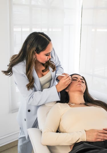 A professional brow artist mapping eyebrows for a microblading procedure in a bright studio.