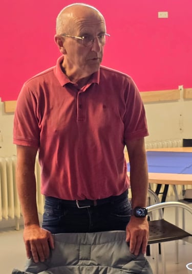 Senior man in a pink polo shirt and glasses standing in a room with a bright pink wall.