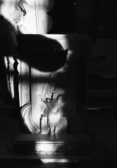 Shadow of the artist in her studio taking a photo of her sculpture half in sunlight, half in darkness.