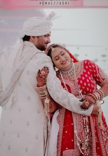 Romantic Indian wedding couple pose, bride in red lehenga leaning on groom in white sherwani. Makeup