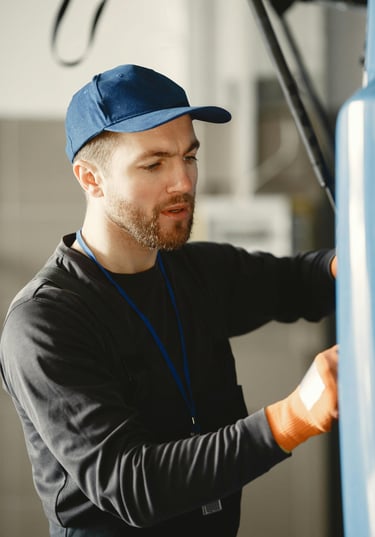Professional mechanic wearing a blue cap and work gloves repairing a vehicle in an auto body shop.