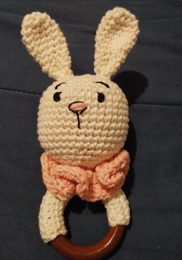 Sonajero de bebé de ganchillo hecho a mano en color crema con forma de conejito y asa de aro madera.