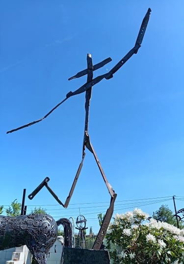 Tall abstract scrap metal sculpture of a human figure outdoors under a clear blue sky.