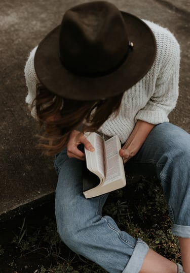 A woman sitting on a sidwalk, thumbing through a Bible